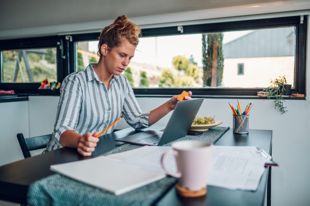 Woman working on laptop in kitchen setting, reviewing freelancer payment documents.