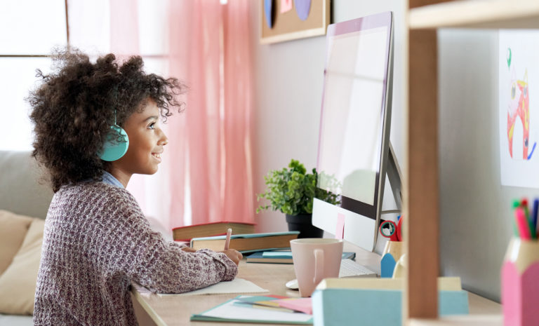 Girl studying online with computer and headphones, illustrating fundamentals of online learning.