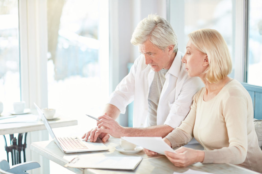 Older couple reviewing financial documents and laptop, planning for life insurance protection.