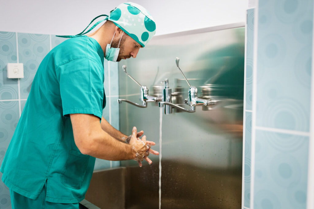 Healthcare worker washing hands thoroughly at hospital sink demonstrating proper hand hygiene techniques.
