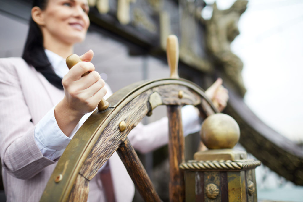 Female leader holding ship's wheel, representing leadership qualities and business management.