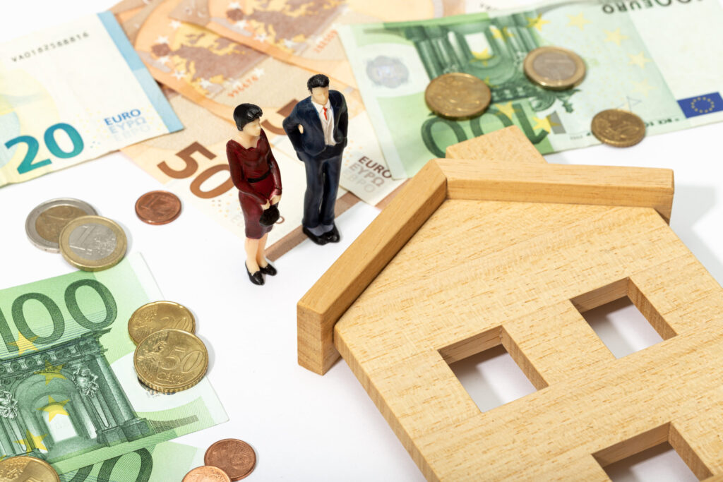 Miniature figures representing investors and a house model surrounded by Euro currency, illustrating real estate investing.