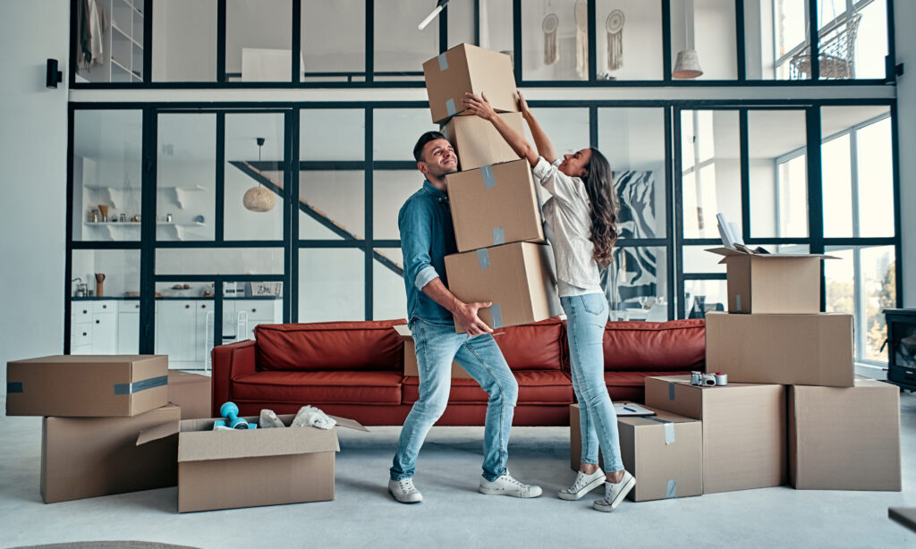 Young couple carrying moving boxes in new home, reducing moving stress.