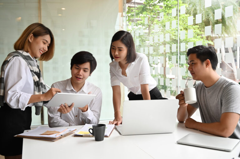 Young business team collaborating and communicating around a tablet and laptop.