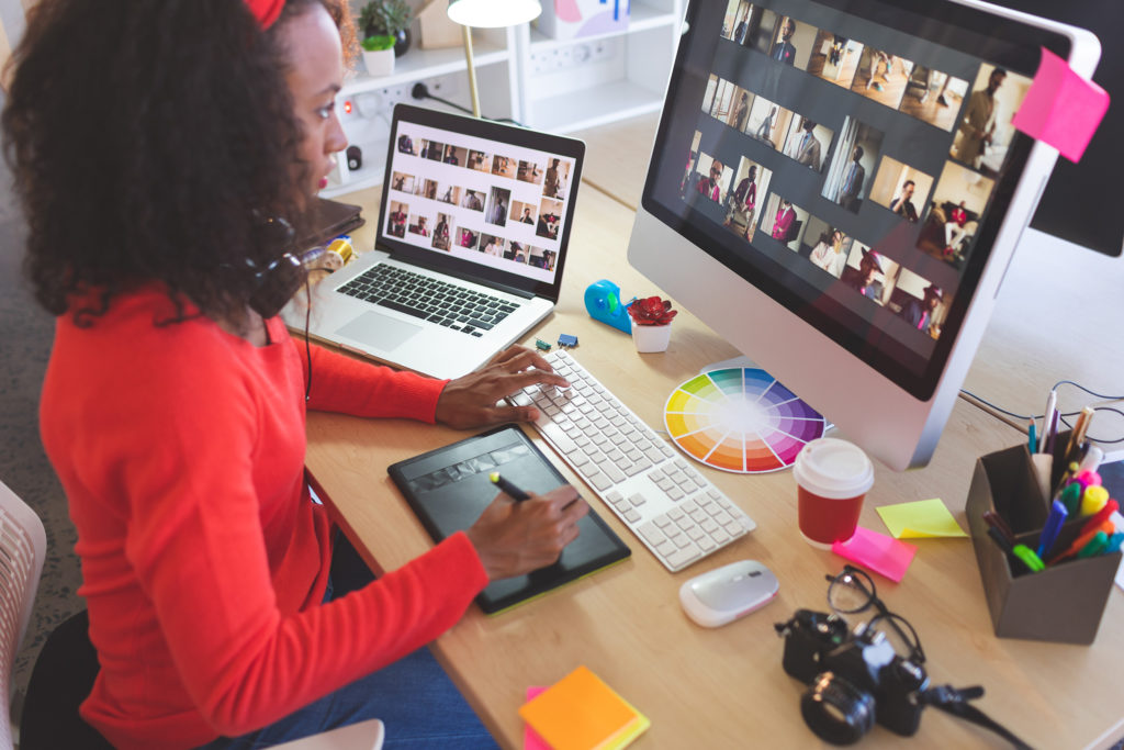 Woman working on laptop and desktop computer designing website layout and graphics.