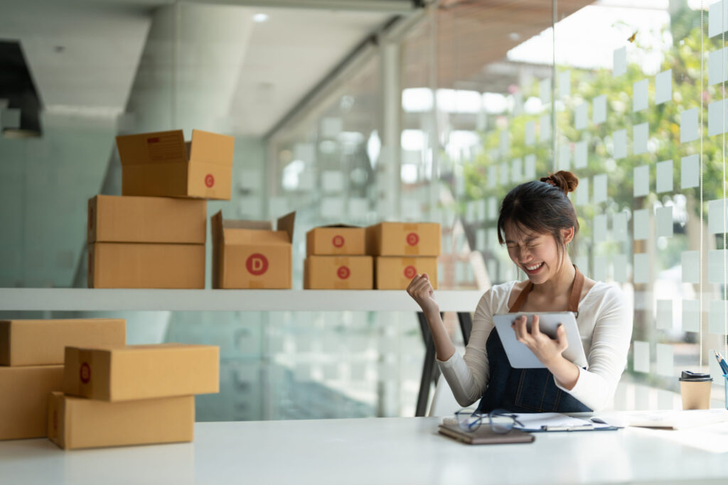 Immigrant entrepreneur celebrating success with tablet and shipping boxes, starting a small business in America